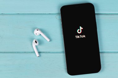 TikTok logo mobile app on screen smartphone iPhone with AirPods on a colored background. TikTok is app to create and share videos. Moscow, Russia -  September 26, 2021