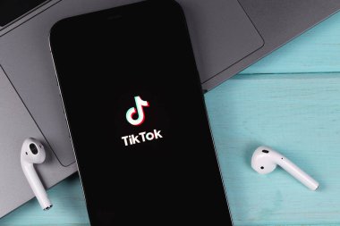 TikTok logo mobile app on screen smartphone iPhone with MacBook, AirPods on a colored background closeup. TikTok is app to create and share videos. Moscow, Russia -  September 26, 2021