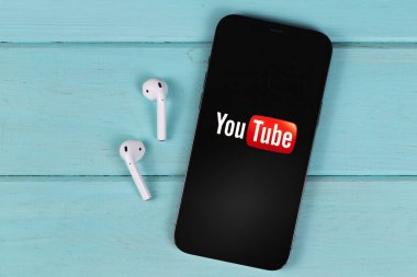 YouTube mobile logo app on screen smartphone iPhone with AirPods on a colored background. YouTube is a free video sharing application that anyone can watch. Moscow, Russia -  September 26, 2021