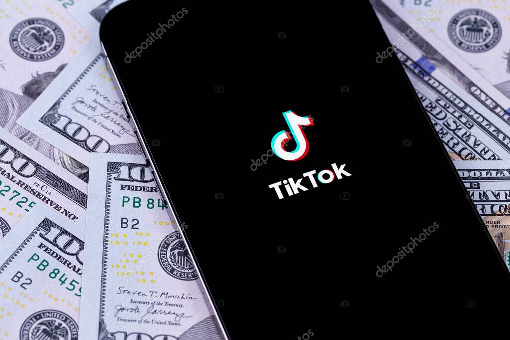 TikTok logo mobile app on screen smartphone iPhone with dollars money closeup. TikTok is app to create and share videos. Moscow, Russia -  September 27, 2021