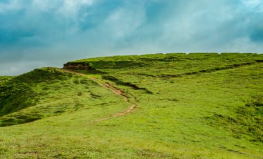 Yeşil tepelerle çevrili bir tepe, mavi gökyüzü ve kopyalama alanı olan yeşil bir tepeye giden bir yol.