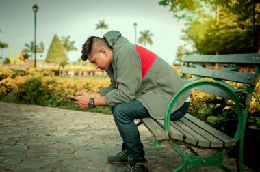 Adam bankta oturuyor, telefonunu kontrol ediyor, genç adam cep telefonunu kontrol ediyor bankta oturuyor.