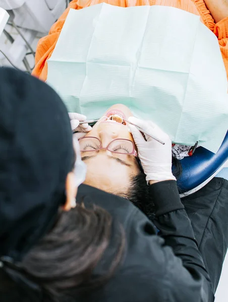 View back of dentist with patient ; Woman dentist doing endodontics to woman patient; Dentist examining mouth to patient; Dentist performing stomatology