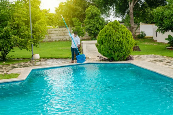 Man cleaning a swimming pool with skimmer, maintenance person cleaning a swimming pool with skimmer, swimming pool cleaning and maintenance concept.