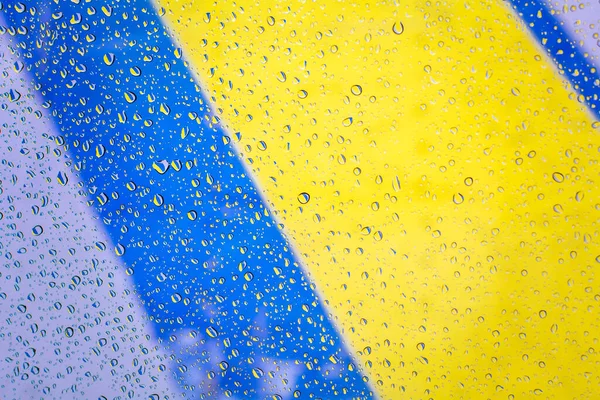 Gotas de lluvia con fondo de bandera de ucrania, gotas de lluvia sobre vidrio con colores de bandera de ucrania. Gotas de agua en la ventana sobre fondo de vidrio