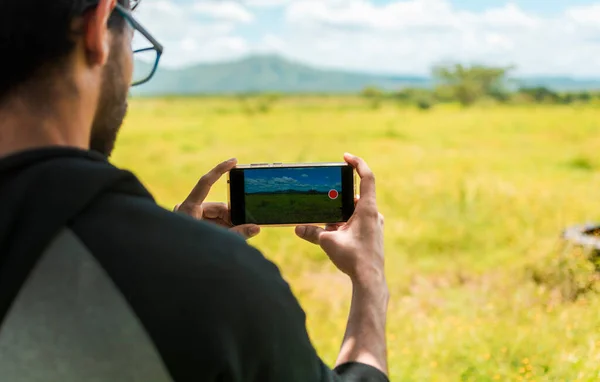 Close up of man hands taking photos of a landscape with the cell phone. Rear view of a person taking a photo of a field with his cell phone, rear view of a man taking photos of a field