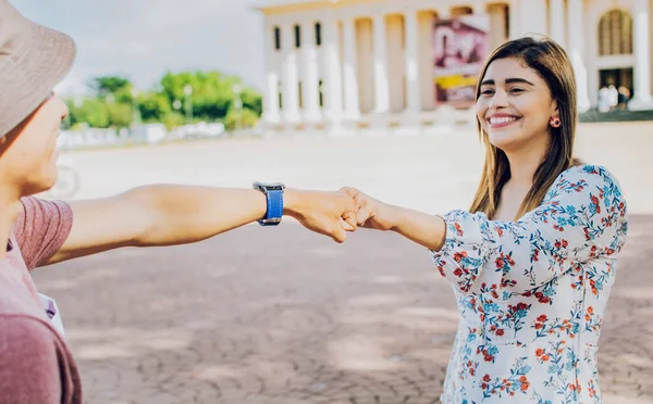 Two young smiling teenagers bumping fists in the street. Close up of guy and girl shaking fists in the street. A guy and girl shaking hands on the street