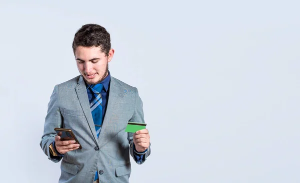 Smiling businessman holding cell phone and credit card isolated. Handsome man with credit card and cell phone in hand isolated, bank payment online concept