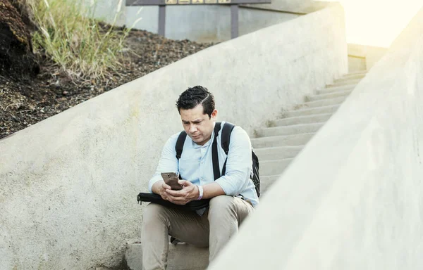 A guy sitting on stairs using his cell phone outdoors with copy space, Young man sitting on stairs using smart phone, Close up of young man sitting on stairs texting on cell phone outdoors