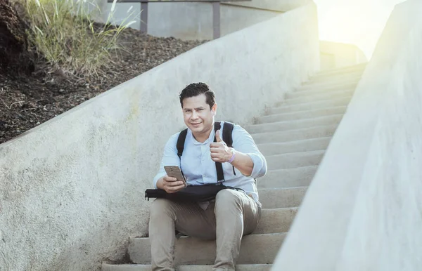 Young man sitting on stairs with cell phone and thumb up, Smiling guy sitting on stairs with cell phone giving thumb up, Close up of person sitting on stairs with cell phone giving thumb up