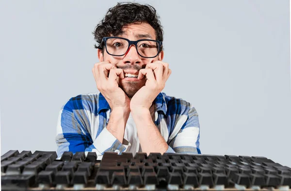 Nervous nerdy guy biting his nails in front of the keyboard, Worried man in glasses at the computer keyboard. Young man worried face in front of keyboard. Man with computer problems