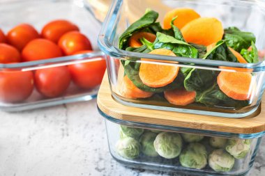 Cam kaplarda çeşitli sebzeler: havuç, ıspanak, domates, Brüksel lahanası. Konteynırlarda vejetaryen yemeği ve atıştırmalıklar, gri arka plan. Temiz yemek, çiğ yemek, detoks, bitki temelli diyet konsepti.