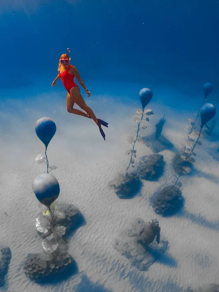 Femme plongeuse libre en maillot de bain rouge, sous l'eau avec des rayons de soleil étonnants et des statues. Plongée sous-marine dans l'océan — Photo