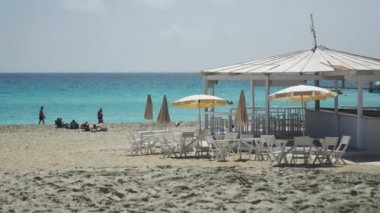 Beyaz güneşli yatak şemsiyeli turistlerin 4K görüntüleri Nissi sahilinde yaz tatili deniz arka planında 