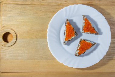 Havyarlı küçük sandviçler, ahşap arka planda beyaz yuvarlak bir tabakta üçgen şeklinde..