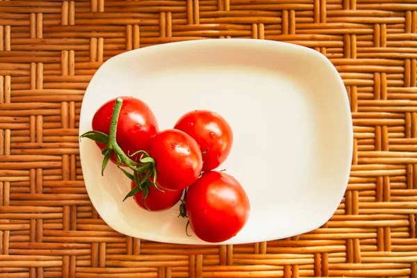 Eine Traube roter Kirschtomaten auf einem weißen flachen rechteckigen Teller steht auf einer hölzernen Weidenfläche. Blick von oben. Horizontales Foto. Lebensstilkomposition. Nahaufnahme — Stockfoto