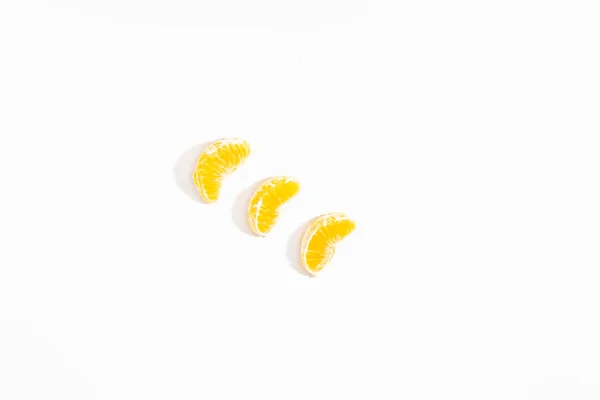 Drie kleine plakjes mandarijn liggen diagonaal op een witte achtergrond. Zicht van bovenaf. Plat gelegd. Isoleer. Levensstijl. Clos omhoog. Horizontale foto. — Stockfoto