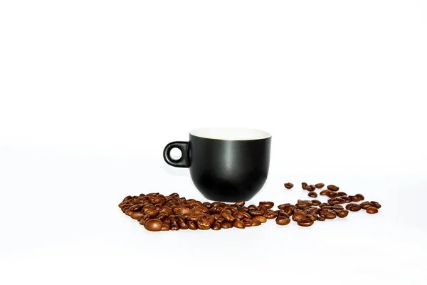 Kleine zwarte hartvormige koffiekop met verspreide bonen op een witte achtergrond. Vooraanzicht. Isoleer. Levensstijl. — Stockfoto