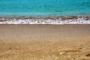 Çakıl taşlı sahilde mavi deniz dalgası.