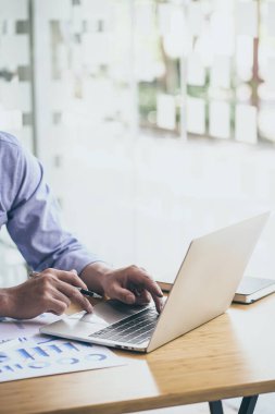 Yeni mimari projesi için dizüstü bilgisayarda çalışan bir iş adamı. Masanın üzerinde genel dizayn defteri var. Bulanık arkaplan, dikey model.