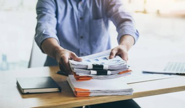 Belge yığınıyla çalışan ve dizüstü bilgisayar kullanan bir iş adamı.