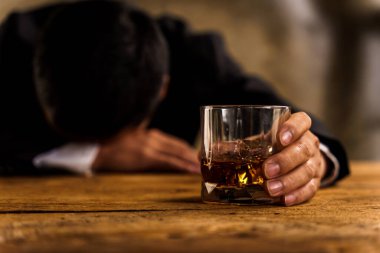 Alkolizm, depresyondaki Asyalı genç adam alkollü içecek içerken masada uyur, geceleri bir bardak viskiyi tek başına tutar. Alkol bağımlılığının tedavisi, taciz sorunu alkolizm kavramı