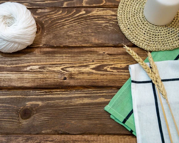 dark wooden boards on which there is a ball of knitting threads, a candle, spikelets of wheat and napkins