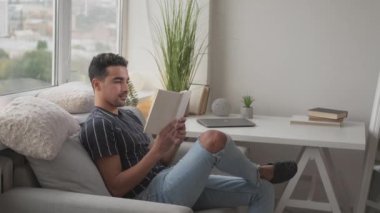 Evde kitap okuyan adam hafta sonunun keyfini çıkarıyor.
