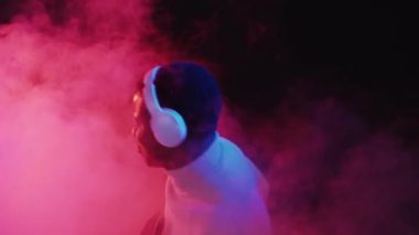 Müzik zevki. Fütürist bir alet. Gece eğlencesi. Kaygısız mutlu adam kulaklıkla dans ediyor. Parlak ışıklı duman efektiyle favori şarkının tadını çıkarıyor..