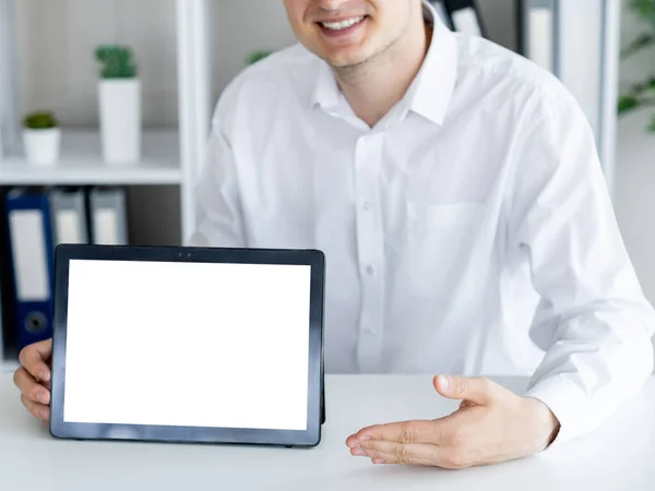 Online presentation. Office man. Computer mockup. Unrecognizable smiling guy pointing to tablet computer with blank screen sitting desk in light room interior.