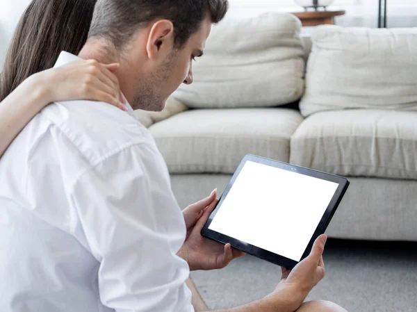 Virtual conference. Family couple. Computer mockup. Unrecognizable man and woman sitting home looking tablet computer with blank screen in light room interior.