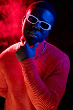 Yakışıklı bir adam. Gece portresi. Modern moda. Kendine güvenen çekici erkek model, şık güneş gözlüklü, neon ışıklı, karanlık stüdyo arka planlı..