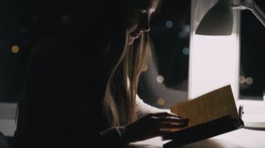 Geç saate kadar çalıştım. Çok çalışan bir öğrenci. Eğitim stresi. Geceleri kitap okuyan yorgun genç kadın karanlık odanın penceresinde sınava hazırlanıyor..