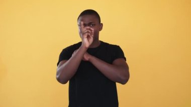 Reddedilme ifadesi. Irkçılık karşıtı. Protesto işareti. Irksal ayrımcılık. Çapraz kollarını gösteren ciddi Afrikalı adam turuncu arka planda izole edilmiş hiçbir parmak hareketini inkar etmez..