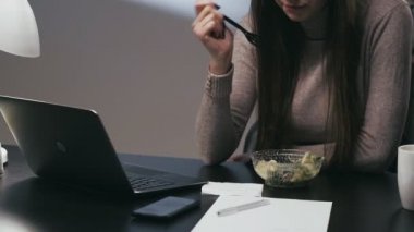 İş yemeği. Ofis yemeği. İş molası. Tanımlanamayan kadın serbest çalışan laptopta geç saatlere kadar çalışıyor ve geceleri çalışma masasında salata yiyor..