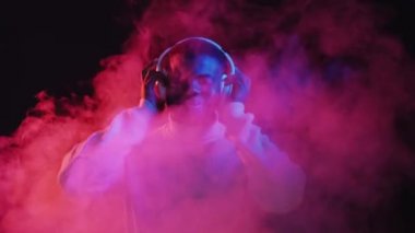 Müzik eğlencesi. Kablosuz kulaklıklar. Gece eğlencesi. Parlak neon ışıklı duman efektiyle synthwave şarkı listesi dinleyen neşeli bir dansçı..