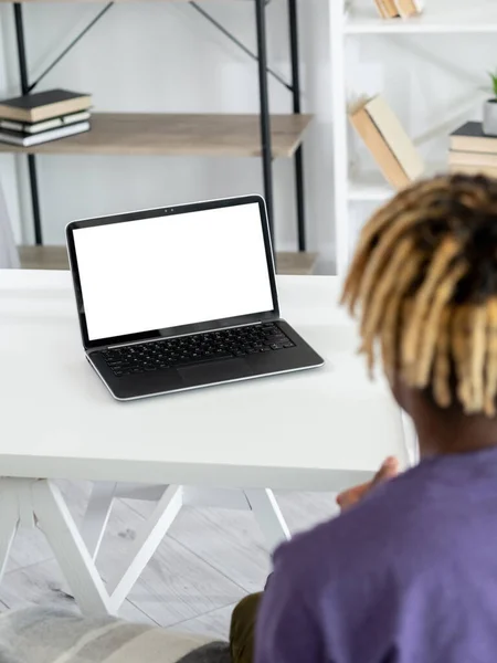 Online conference. Black man. Digital mockup. Unrecognizable guy sitting work desk looking laptop blank screen in light room interior.