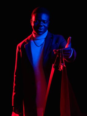 Alışveriş alışverişi. Kara Cuma. Mağaza satışı. Özel fiyat. Elinde renkli kırmızı neon ışıklı arka planda alışveriş torbaları tutan memnun bir adam..