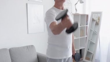 Spor malzemeleri. Evde spor salonu. Dayanıklılık. Kapalı alanda egzersiz aletleri. Tanınmayan atletik adam, hafif iç organlarında dambıllar olan kol kaslarını çalıştırıyor..