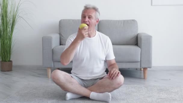 健康的营养 健康饮食 抗氧化脱氧剂 在现代家居生活中 有运动动机的中年男人喜欢盘腿坐在地板上吃新鲜的绿色苹果 — 图库视频影像