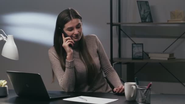 办公室经理 移动通信 企业生活方式 快乐的女秘书在笔记本电脑黑暗的写字台上用电话交谈 — 图库视频影像