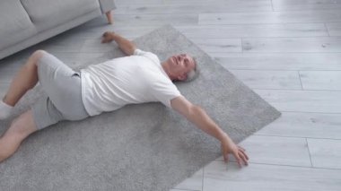 Pilates egzersizi. Evde fitness. Kuvvet esnekliği. Sağlığın için. Rahat orta yaşlı bir adam halının üzerine uzanmış yatıyor..