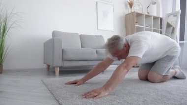 Evde yoga. Pilates eğitimi. Sabah sporu. Rahatlamış orta yaşlı bir adam oturma odasının iç kısmında boyun germe kasları egzersizi yapıyor..