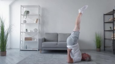 Evde eğitim. Kapalı spor salonu. Dayanıklılık. Atletik orta yaşlı bir adam oturma odasının içinde şamdan egzersizi yapıyor..