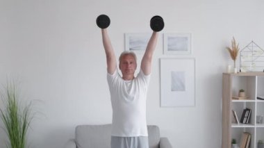 Evde eğitim. Sabah sporu. Ağırlık kaldırma. Güçlü orta yaşlı bir adam hafif modern iç mekanlarda kol kasları için fiziksel egzersiz yapıyor..