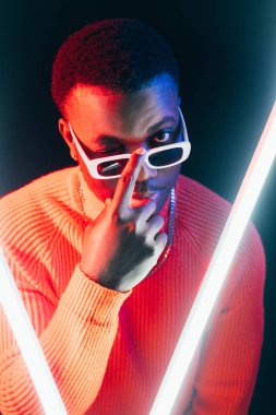 Maço adam. Gece kulübü hayatı. Retrodalga tarzı. Moda güneş gözlükleriyle göz kırpan şık flörtçü adamın portresi. Karanlık arka planda LED ışığı..