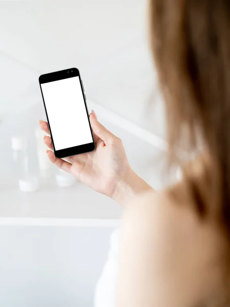 Online communication. Digital mockup. Virtual life. Unrecognizable woman holding smartphone with blank screen in light bathroom interior blur.