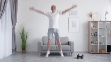 Evde fitness. Kapalı alanda eğitim. Aktif yaşam tarzı. Orta yaşlı atletik bir adamın hafif oturma odasında atlama egzersizi yapması ilham verici..