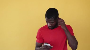 Müzik uygulaması. Mp3 çalma listesi. Gadget insanları. Modern teknoloji. Kablosuz kulaklık takan tatmin olmuş Afrikalı adam portakal fotokopi arkaplanından izole edilmiş cep telefonundan keyif alıyor..