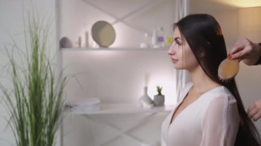 Saç stili tamiri. Güzel kadın. Sağlıklı tedavi. Tanımlanamayan bir kadın, açık renkli iç mekanda uzun, düz, esmer saçları tarıyor..